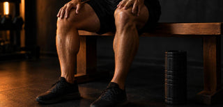 Sportif assis sur un banc après une séance de jambes, mains sur les cuisses, rouleau de massage posé au sol