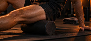 Cuisse d'un sportif posée sur un rouleau de massage noir sur un tapis, pour soulager les courbatures après la séance