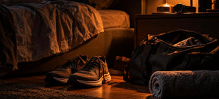 Chaussures de running et sac de sport au pied d'un lit dans une chambre sombre, après une séance de sport le soir
